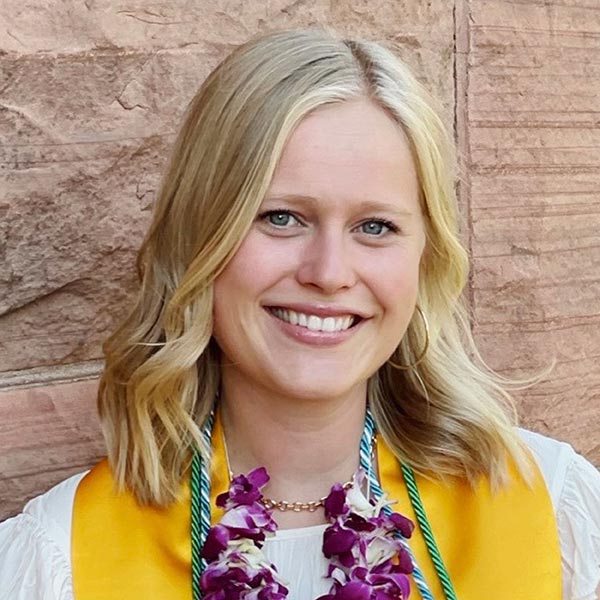 Headshot of Avery Bell. Avery is smiling, with shoulder-length blonde hair and a white and yellow shirt with a flower necklace.