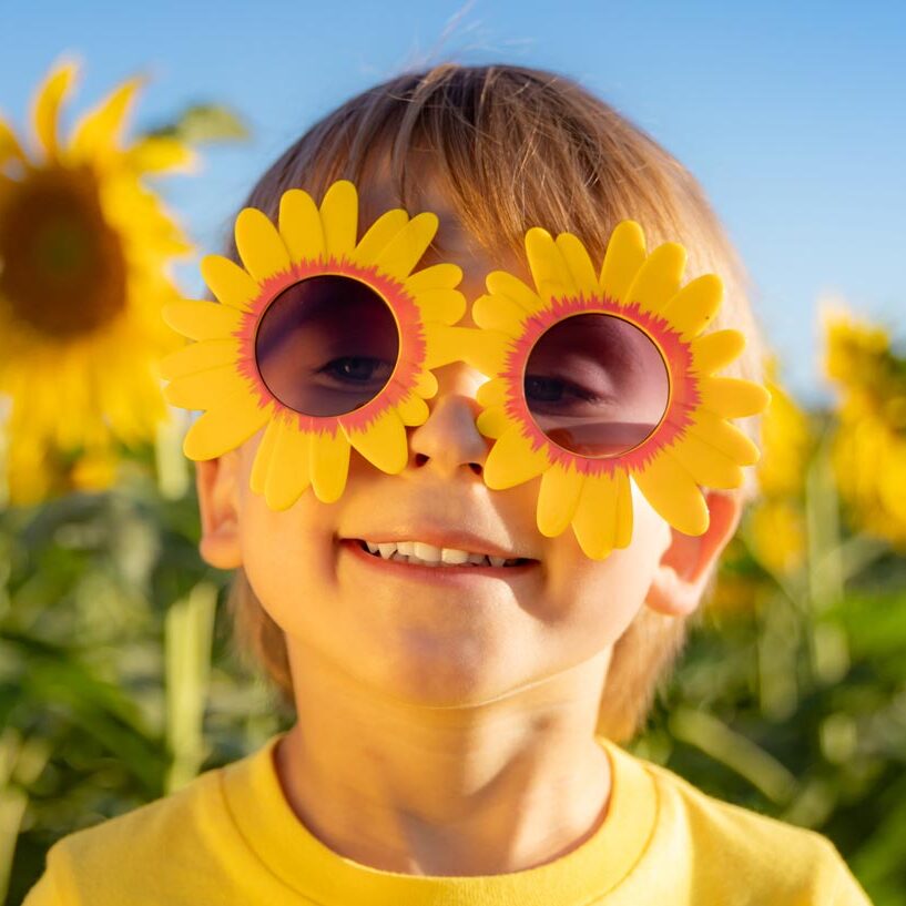 Young child wears sunflower glasses while standing in a sunflower field