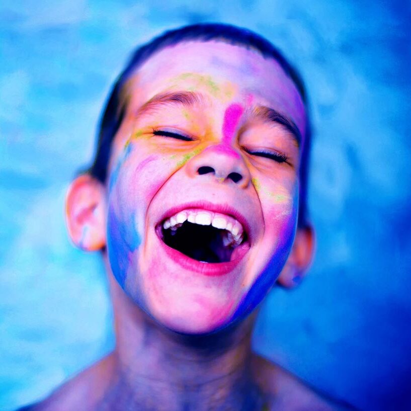 Boy wearing face paint laughs against a blue background