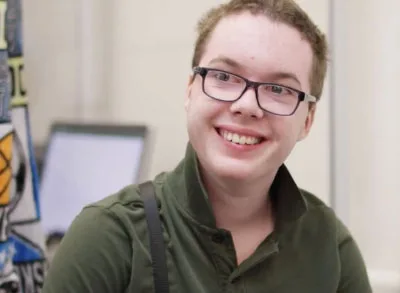 3.3.23_SpreadingPosP Autistic white teenage boy with a green polo and glasses smiling in his classroom.