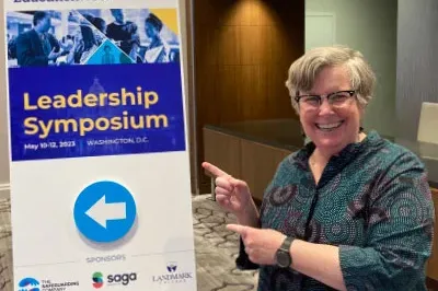 5.17.23_EdWeekPW Patricia Wright, Proof Positive Executive Director, is smiling and pointing at the Education Week Leadership Symposium conference poster.