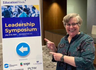 5.17.23_EdWeekPW Patricia Wright, Proof Positive Executive Director, is smiling and pointing at the Education Week Leadership Symposium conference poster.