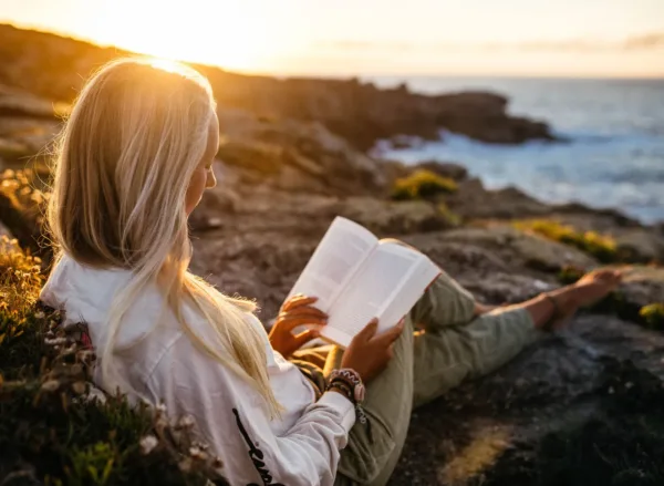 Positive Psychology Summer Reading Reccomendations A woman is reading on the beach during sunset.