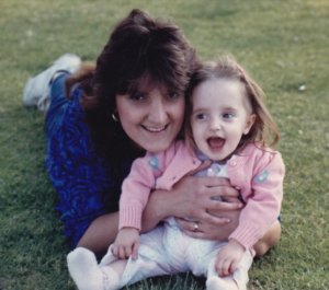 A young Nicole embracing her mother while lying on the grass.