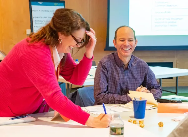 400x293_LeanIntoLearning_2 (1) Woman in pink sweater and man in green button up laughing while writing on a poster in a conference room.