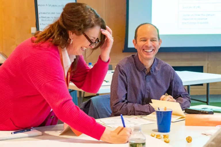 400x293_LeanIntoLearning_2 (1) Woman in pink sweater and man in green button up laughing while writing on a poster in a conference room.