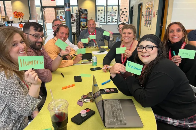 400x293_Nicole_New A group of teachers at a yellow table are holding up signs with character strengths on them for a professional development.