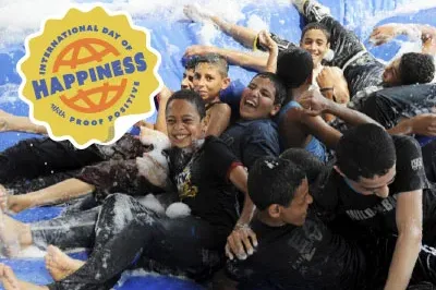 400x293_IDOH_PressRelease-Blog Group of middle school boys in a foam bounce inflatable smiling with logo: International Day of Happiness with Proof Positive