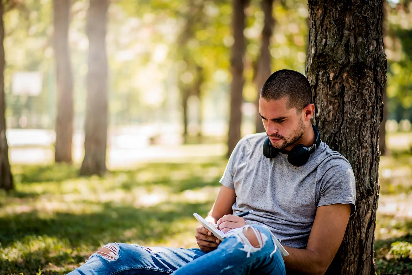 a man leaning against a tree writing a letter