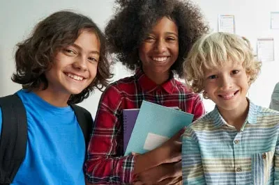 HappySchools Three young kids, older elementary-aged, smiling and holding notebooks.