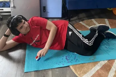 400x293_EPICMindMed_1 An autistic student is relaxing on his yoga mat. He is lying on his side with this hand propping his head up.