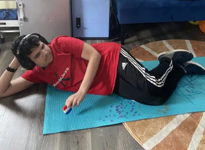 400x293_EPICMindMed_1 An autistic student is relaxing on his yoga mat. He is lying on his side with this hand propping his head up.