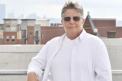 Johanna is standing with a city backdrop wearing a white button up shirt with sunglasses on.