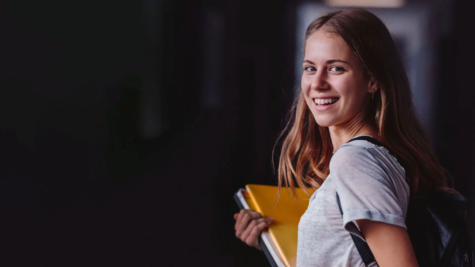 Join the Alliance. A teenager is holding schoolbooks and smiling