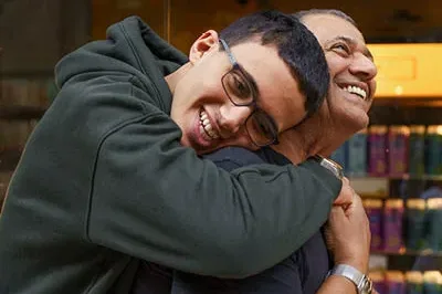 400x293_EvergreenBlogPic A son is hugging his father with his arms wrapped around the father's back. They are smiling