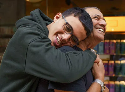 400x293_EvergreenBlogPic A son is hugging his father with his arms wrapped around the father's back. They are smiling
