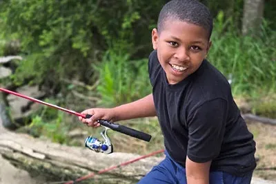 400x293_Mr.Fisherman2 Asante is smiling and sitting on a log with his fishing rod in his hand