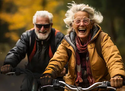 400x293_HappyHabitBikers Two elder people, a man and a woman, riding bikes with big smiles.