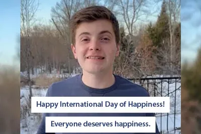400x293_Sebastian_IDOHEveryoneDeserves A young autistic man standing in front of trees. Blue copy on top of white box that says "happy international day of happiness! Everyone deserves happiness."