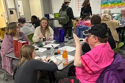 400x293_InsightBehaviorIDOH Pictures shows people sitting at a table laughing and filling out and coloring worksheets with a sun that represents what they're grateful for.