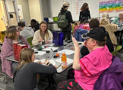 400x293_InsightBehaviorIDOH Pictures shows people sitting at a table laughing and filling out and coloring worksheets with a sun that represents what they're grateful for.