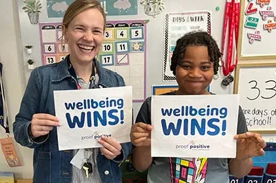 400x293_ManifestoBlogPic Picture shows a teacher and student smiling and holding up signs that say "wellbeing wins!"