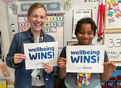 Picture shows a teacher and student smiling and holding up signs that say 