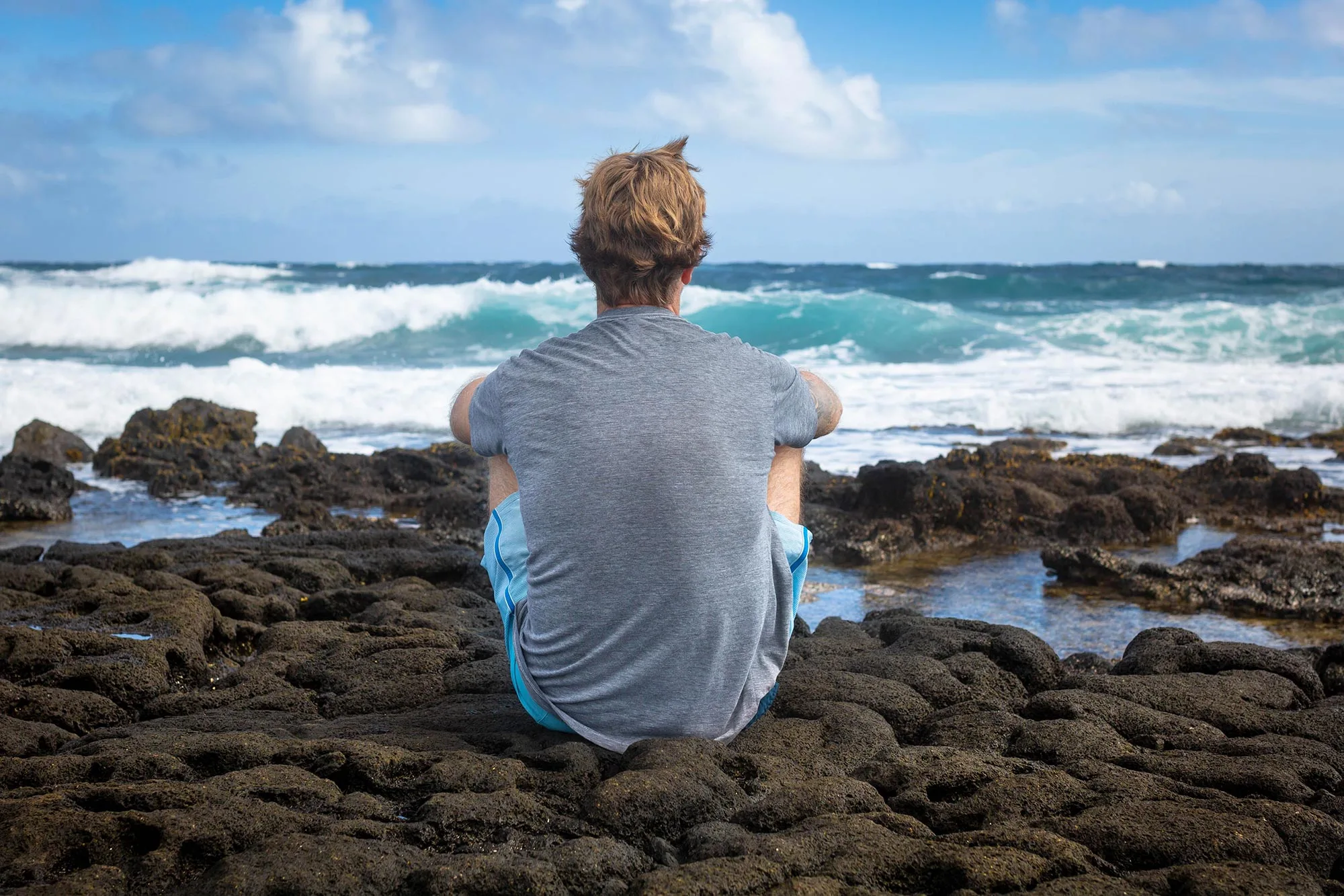 a young man sitting on rocks looking at the ocean