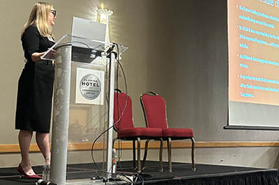 Paige Raetz is at the podium presenting at a professional conference.